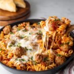 A skillet filled with a delicious Dump and Bake Meatball Casserole, topped with melted cheese and garnished with parsley, ready to be served with crusty bread.